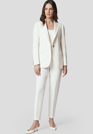 Biała dopasowana marynarka z zapięciem na guziki, w zestawie z dopasowanymi spodniami. Noszona z białymi szpilkami, charakteryzująca się gładkim materiałem i czystymi liniami.