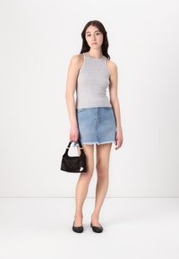 Gray sleeveless top, denim mini skirt with frayed hem, black textured handbag, and black flat shoes. Model poses against a plain background.