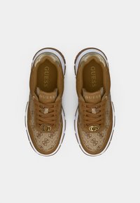 Καφέ αθλητικά παπούτσια με μπεζ επάνω μέρος με σχέδιο, χρυσές λεπτομέρειες και λευκές σόλες. Διαθέτουν λογότυπο στο πλάι και κορδόνια με υφή.