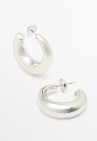 Silver hoopsringar med en slät, polerad yta, som har en böjd design och stiftbakgrund för säker användning.