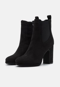 Bottes chevilles en daim noir avec un talon épais, des panneaux latéraux élastiques et une fermeture éclair. Texture lisse avec un design à bout rond.