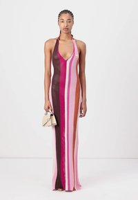 Strikket maxikjole med dyp V-hals, med vertikale striper i rosa, brunt og kremfarge. Modellen holder en liten beige håndveske.