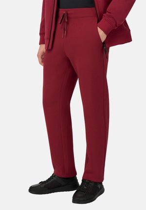 Bordeaux sportbroek met een elastische tailleband, trekkoordsluiting, zijzakken en taps toelopende pijpen. Gecombineerd met zwarte sneakers.