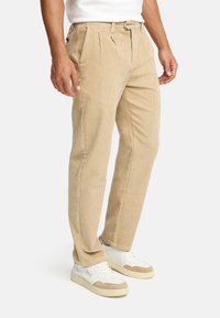 Beige corduroy trousers with pleats, featuring side pockets and a straight leg design. Paired with white and tan casual sneakers.