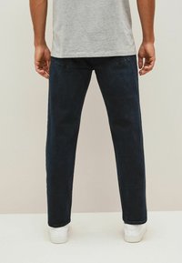 Donkerblauwe denim jeans met een recht gesneden ontwerp, met achterzakken en gecombineerd met witte sneakers. De stof heeft een gladde textuur.