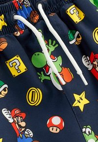 Marinfärgad badshorts i tyg med tryck av tecknade figurer, som Yoshi, Mario och olika spelikoner. Vit dragsko och slät textur.