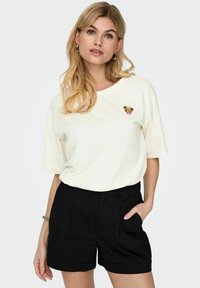 Off-white t-shirt met korte mouwen, voorzien van een kleine berenafbeelding op de borst, gecombineerd met hoge zwarte shorts met plooien.