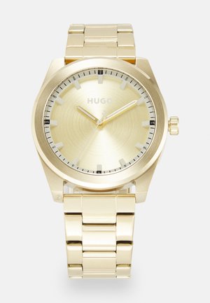 Montre-bracelet de couleur or avec un boîtier rond, un cadran texturé, des aiguilles luminescentes, un bracelet en acier inoxydable et des index noirs.