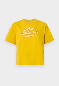 Kollane lühikeste varrukatega puuvillane T-särk, millel on suur heledat tooni "New Balance" logo koos kõverjoonega alljoone detailiga.
