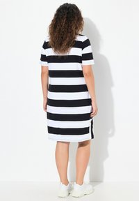 Schwarz-weißer gestreifter Kleid mit kurzen Ärmeln und Seitenschlitzen, aus einem dehnbaren Stoff, der bis zur Mitte des Oberschenkels reicht.