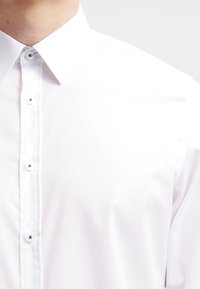 Camicia bianca con bottoni, dotata di un colletto classico, texture liscia e bottoni decorativi neri lungo il giromanica.