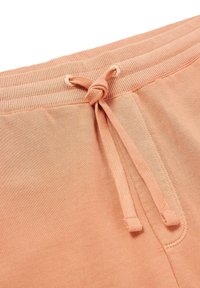 Pfirsichfarbene Sweatpants mit einer weichen Textur, die einen gerippten Bund und einen Kordelzug mit einem geknoteten Detail aufweisen.