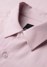 Chemise rose clair à col avec des boutons blancs, soigneusement pliée pour montrer le col et les boutons supérieurs.
