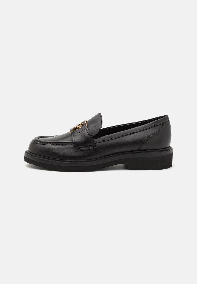 Mocassin en cuir noir avec talon bas et détail en métal doré sur le dessus, présenté de profil sur un fond uni.