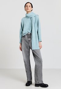 Hellblauer Strickpullover mit einem Schal, kombiniert mit hochtaillierten, lockeren grauen Denim-Jeans und schwarzen Ankle-Boots.