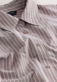 Chemise marron clair avec des fines rayures verticales blanches, des boutons beige et un col classique posé à plat.
