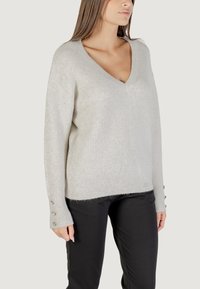 Maglione a coste grigio chiaro con scollo a V e maniche lunghe. Presenta bottoni decorativi sui polsini. Materiale morbido e testurizzato. Vestibilità casual.