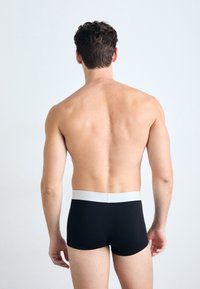 Sorte boxer briefs med en hvid taljeelastik, glat stof, tætsiddende design og kort snit, vist fra ryggen.