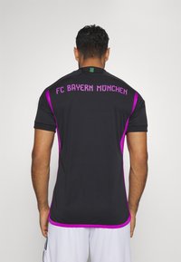 Svart sporttröja med lila detaljer. "FC Bayern München"-logotypen tydligt synlig på baksidan. Korta ärmar och rund halsringning.