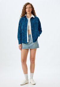 Blå mönstrad oversized skjorta med blommönster, vit skjorta med krage under, denim minikjol, vita sneakers och grå strumpor.