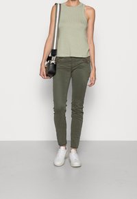 Jasnozielony, prążkowany top bez rękawów zestawiony z oliwkowymi, dopasowanymi spodniami. Białe sneakersy i mała czarna torba na ramię z paskiem w paski.