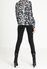 Blouse à motifs noir et blanc avec manches bouffantes, dos à découpe en forme de trou de serrure, associée à un pantalon noir ajusté et des bottes zippées montantes jusqu'aux genoux.