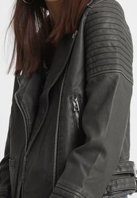 Czarna skórzana kurtka motocyklowa z pikowanymi detalami na ramionach, asymetrycznym zamkiem błyskawicznym i srebrnymi elementami ozdobnymi.