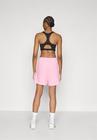 Fekete sportmelltartó versenyháttal, pink sportnadrággal párosítva. Fehér zokni és sportcipő egészíti ki az öltözéket.