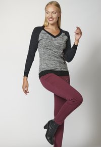 Graues und schwarzes langärmliges V-Ausschnitt-Oberteil mit strukturiertem Körper, kombiniert mit burgunderfarbenen schmalen Hosen. Schwarze Knöchelstiefel runden das Outfit ab.