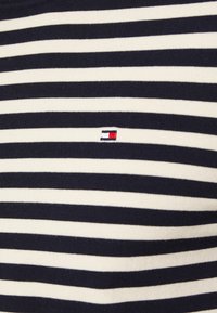 Pull rayé bleu marine et blanc en tissu tricoté, avec un petit logo de marque sur la poitrine. Col rond classique.