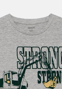 Sivý bavlnený tričko s okrúhlym výstrihom. Obsahuje zelený grafický nápis "SILNÝ" a ilustráciu stavebného vozidla s predĺženou rukou.