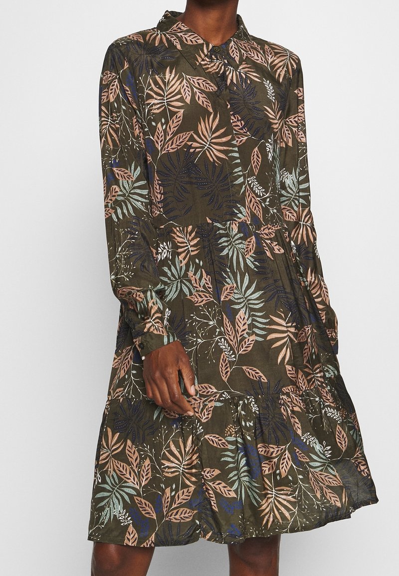 Zielona sukienka w kwiaty z długimi rękawami, zapięciem na guziki przy kołnierzu, z falbanami warstwowymi na dole, ozdobiona różowymi, niebieskimi i białymi wzorami liści na lekkim materiale.