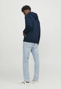 Sudadera navy con bolsillo tipo canguro y capucha con cordón, combinada con jeans de un tono azul claro y zapatillas blancas con detalles negros.