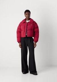 Κοντό πούφφερ μπουφάν σε σκούρο κόκκινο χρώμα, με κουμπιά μπροστά, φαρδύ γιακά και ραμμένη σχεδίαση. Συνδυασμένο με μαύρα παντελόνια σε φαρδιά γραμμή.