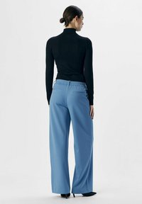 Blå vide benbukser med elastisk talje, parret med en tætsiddende sort turtleneck. Glat tekstur, minimal detaljer og ingen synlig hardware.
