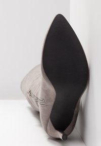 Bota gris texturizada hasta el tobillo con punta afilada, tacón delgado y suela de goma negra con surcos horizontales para mayor agarre.