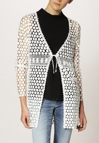 Vit stickad cardigan med blommönster, öppen frontdesign, trekvartslånga ärmar och knytning i midjan.