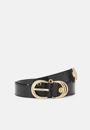 Cinturón negro de cuero texturizado con hebilla dorada ornamentada y múltiples anillos dorados sobre un fondo liso y claro.