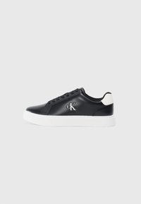 Tenis negri din piele cu talpă albă, vârf rotund, cinci găuri pentru șireturi și un logo argintiu "cK" pe partea exterioară. Accente texturate pe călcâiul alb.