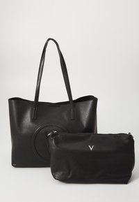 Svart läderhandväska med långa handtag, med en cirkulär präglad design. Inkluderar en mindre svart väska med dragkedja och en silverfärgad logotyp.