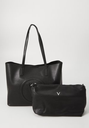 Mustavärinen nahkakassi, jossa on kaksi kantohihnaa ja kohokuvioitu pyöreä kuvio. Mukana on pienempi musta vetoketjupussi, jossa on hopeinen logo.