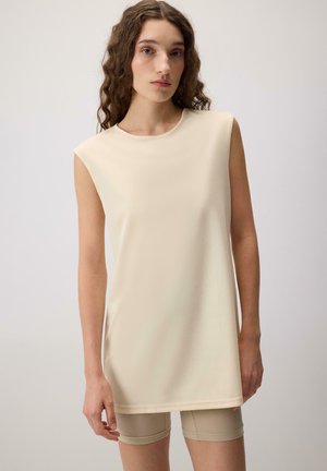 Tunique sans manches beige en tissu léger et doux, avec un col rond et une coupe droite, associée à un short beige.