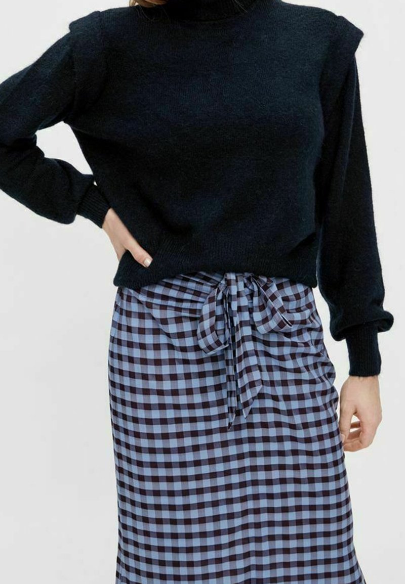 Black knit sweater with turtleneck and puffed sleeves, paired with a blue and black checkered skirt, featuring a tied waist detail.
