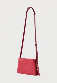 Punane nahast risti üle õla kott, millel on reguleeritav rihm ja kuldsetest detailidest aktsendid. Sile tekstuur, ristkülikukujuline kuju, minimalistik disain.