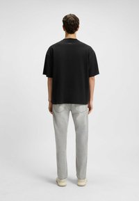 Black oversized t-shirt with short sleeves, featuring a simple design and a small logo at the back neckline, paired with light gray jeans.