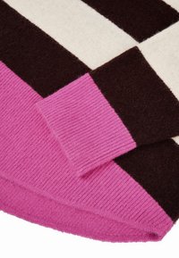 Neulepaita, jossa on ruskean, kermaisen ja vaaleanpunaisen raitakuosi, jossa on vaaleanpunaiset ribbauskaulat ja pehmeä, teksturoitu villakankainen sekoitus.