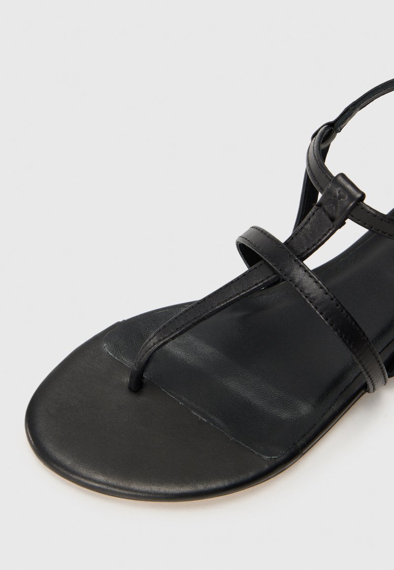 Sandali neri in pelle con suola piatta, design a T con due cinghie sottili e superficie liscia sulla soletta.