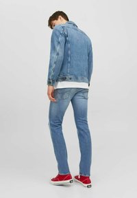 Chaqueta de denim en azul claro con un diseño ajustado, combinada con jeans azul claro y zapatillas rojas. Presenta costuras visibles y bolsillos traseros.