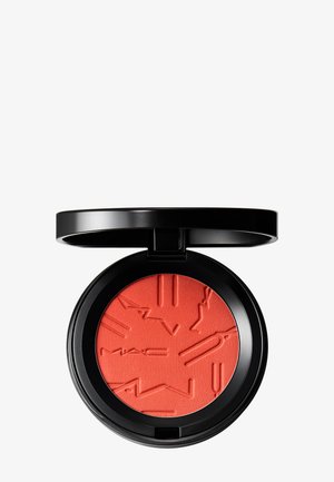 Étui compact noir contenant un blush poudre corail vif avec logo MAC embossé et design abstrait, couvercle ouvert sur fond blanc.