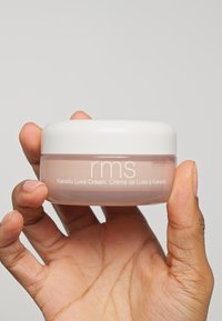 Crème Kakadu Luxe dans un pot rond en verre transparent avec un couvercle blanc, contenant une crème rose douce à l'intérieur et le nom de la marque "rms" affiché en évidence.